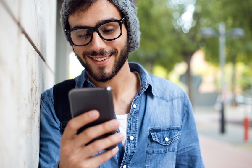 Young man smiling while viewing a mobile-optimized B2B email on his smartphone outdoors, demonstrating responsive design and user-friendly interface.