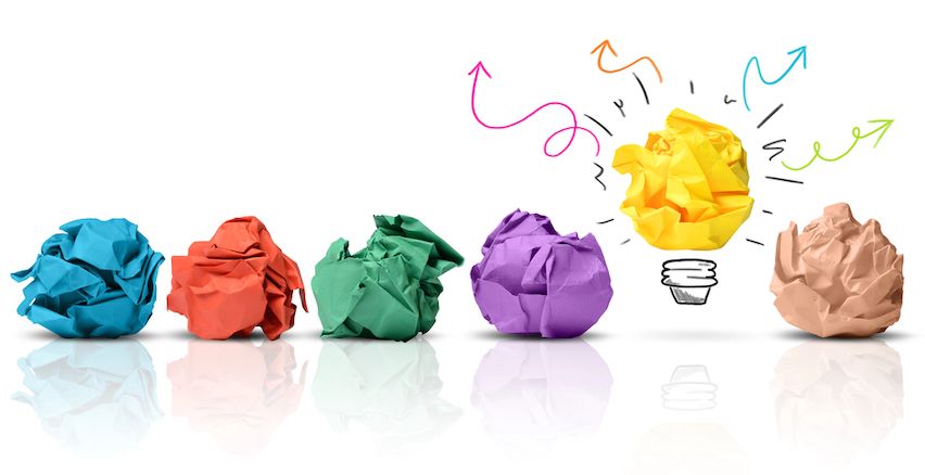 Crumpled paper balls and a bright lightbulb drawing, depicting the evolution of a creative idea.