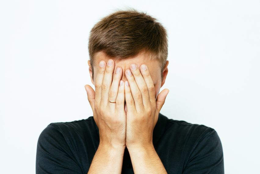 Man covering face with hands, symbolizing regret over using an inappropriate email sign off.