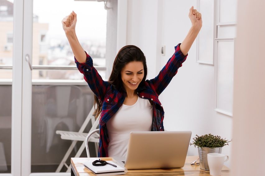 Joyful woman with brown hair in victory pose at her desk, celebrating email marketing success.