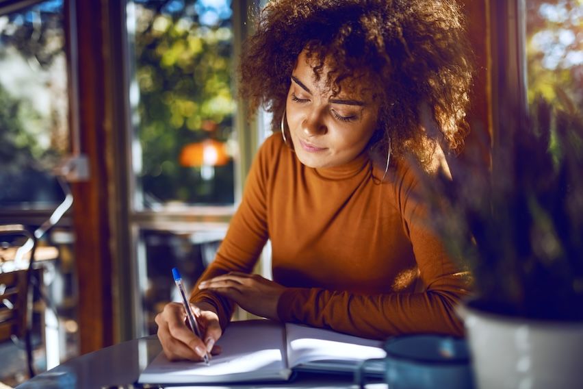 Young woman crafting a message in a notebook, symbolizing thoughtful email content creation.