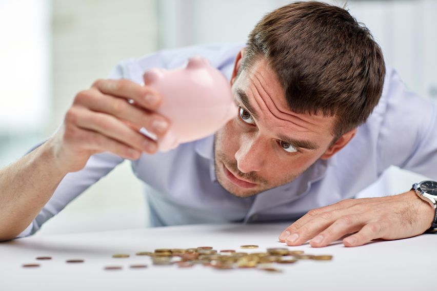 Businessman emptying a piggy bank, searching for coins, illustrating cost savings in targeted engagement.