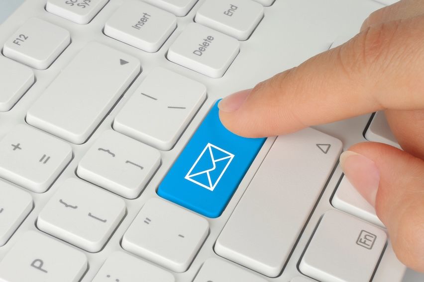 Hand pressing a key with an envelope icon on a keyboard, symbolizing the sending of an email campaign
