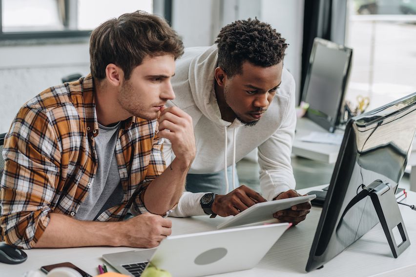 Two young men at a desk, both focused on a monitor, symbolizing indie hackers and bootstrappers working together.