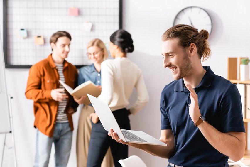 Happy man with notebook symbolizing success in email marketing, with colleagues discussing at a whiteboard behind