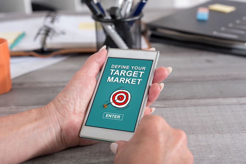 Hand holding mobile showing 'Define your target market' with a bullseye target and arrow, highlighting segmentation.